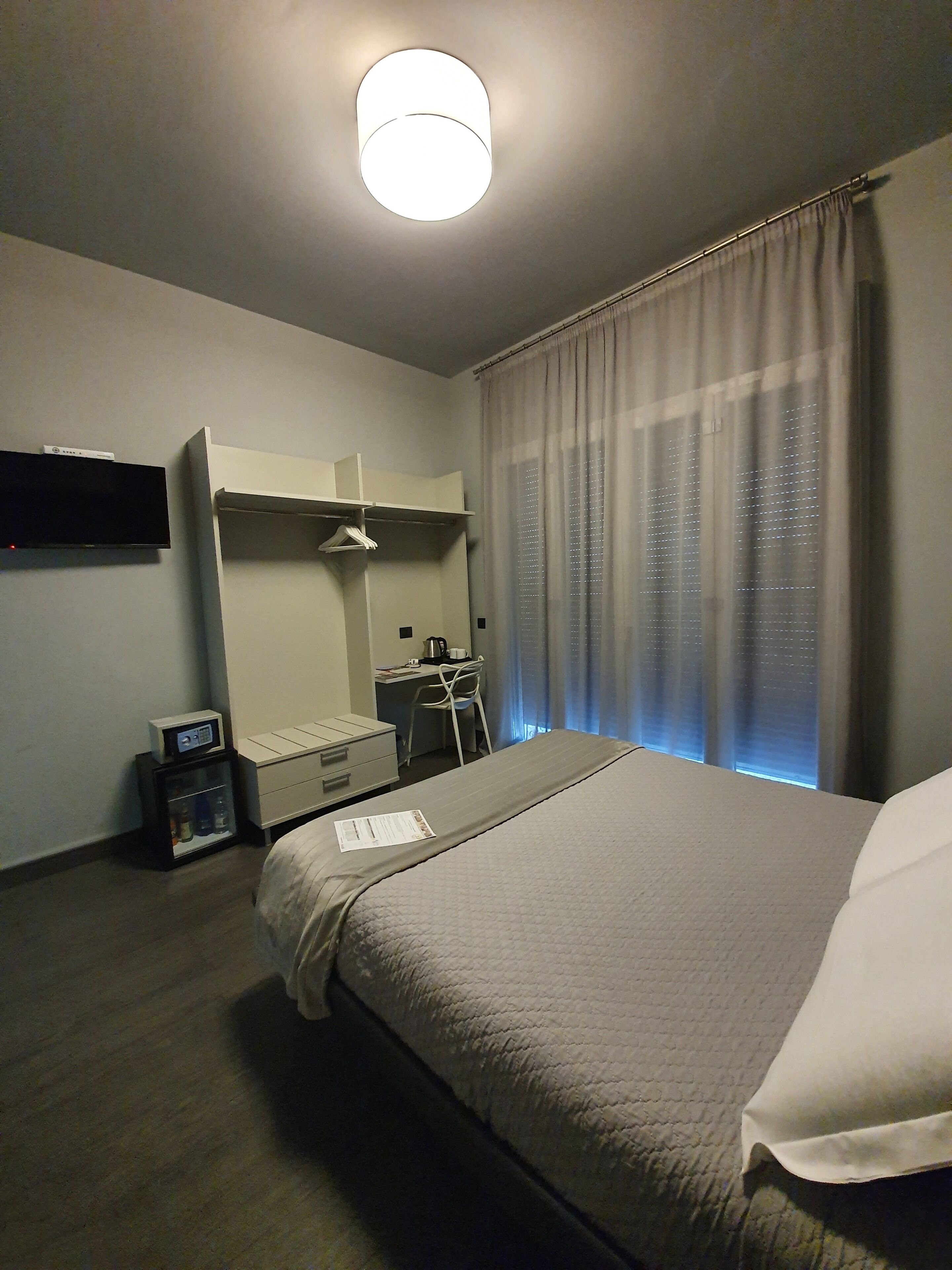 A hotel room with a bed, a desk, a chair, a flat-screen TV, and a window with curtains.