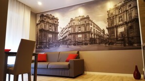 Un salón con un gran mural de un paisaje urbano en la pared, un sofá con cojines rojos y suelo de madera.