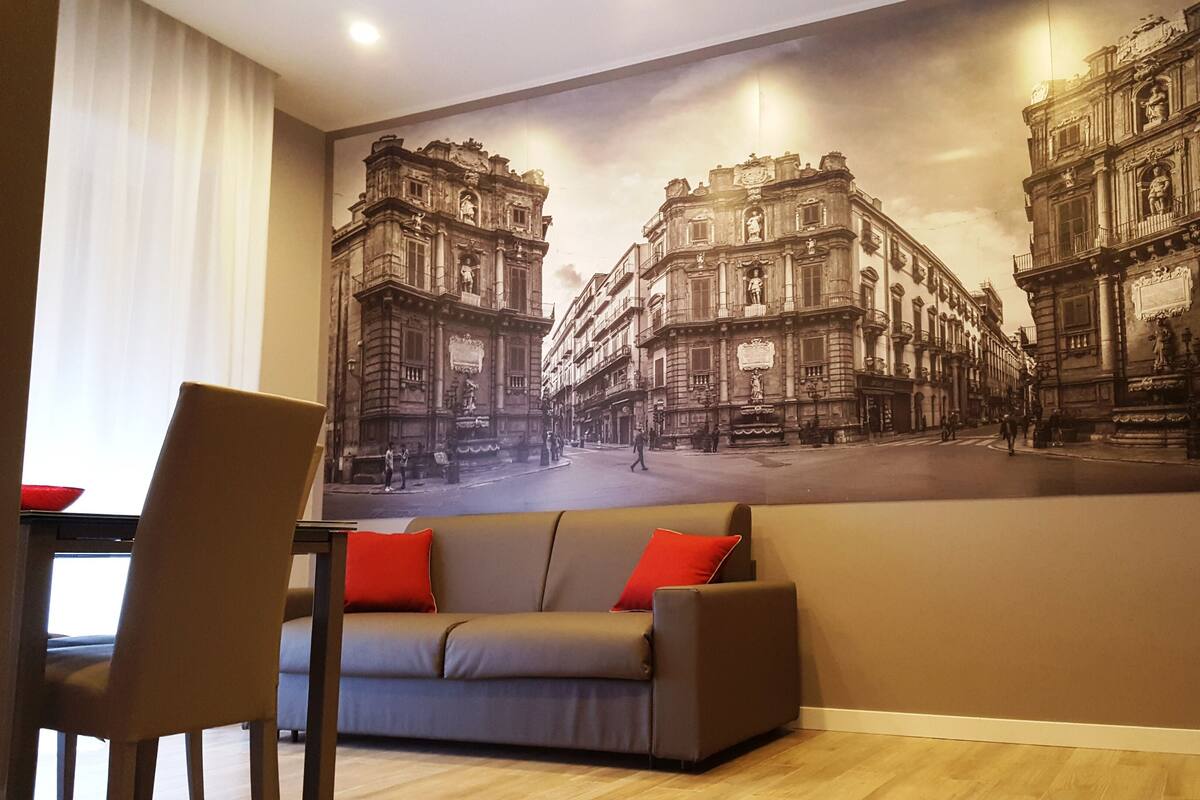 A living room with a large cityscape mural on the wall, a sofa with red cushions, and a wooden floor.