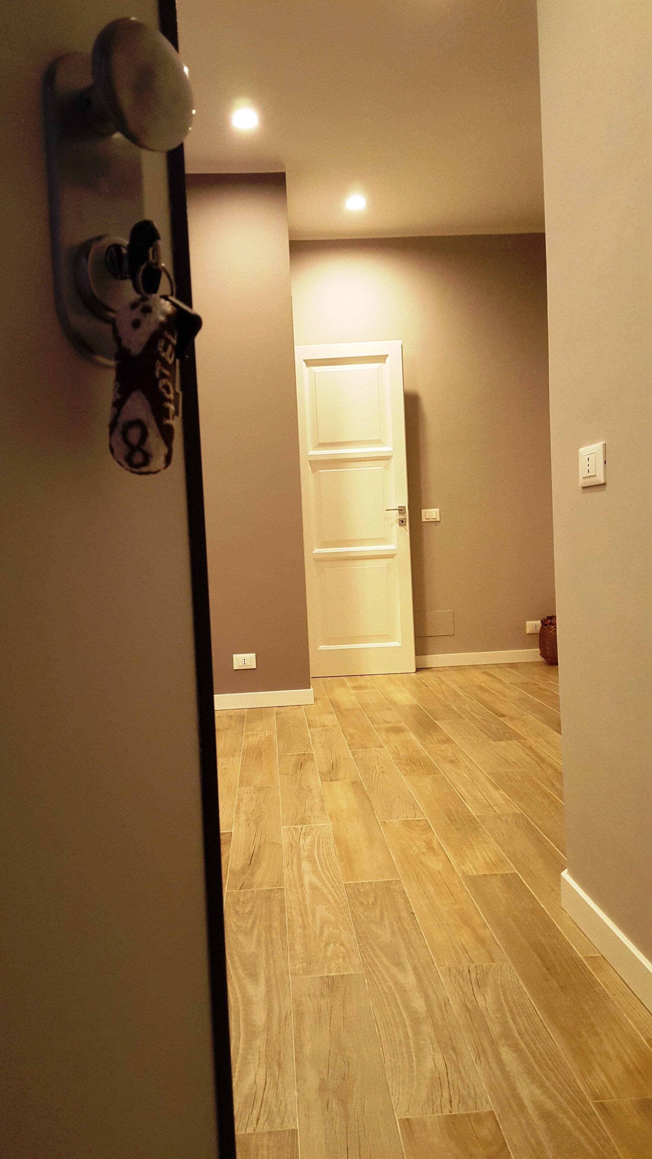 Un couloir d’hôtel avec un plancher en bois, une porte blanche et un lecteur de carte magnétique fixé au mur.