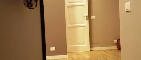 Un pasillo de hotel con suelo de madera, una puerta blanca y un lector de tarjetas de acceso en la pared.