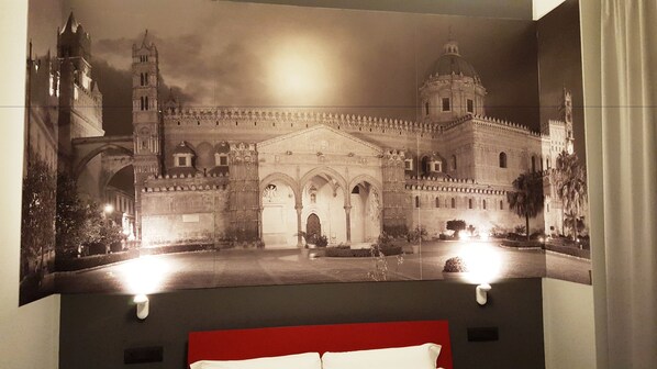Habitación de hotel con un cartel grande de un edificio histórico, cabecera de cama roja y una ventana pequeña.