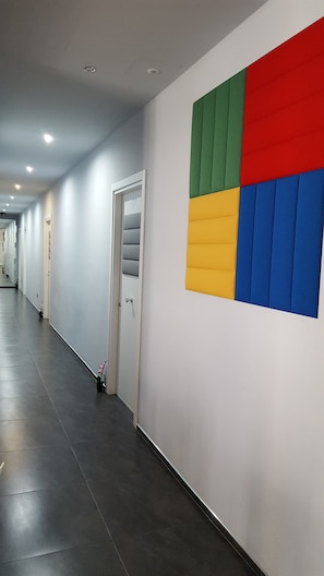 A hallway with a white door, a wall with a colorful geometric design, and a tiled floor. - Alma Hotel (Palermo)