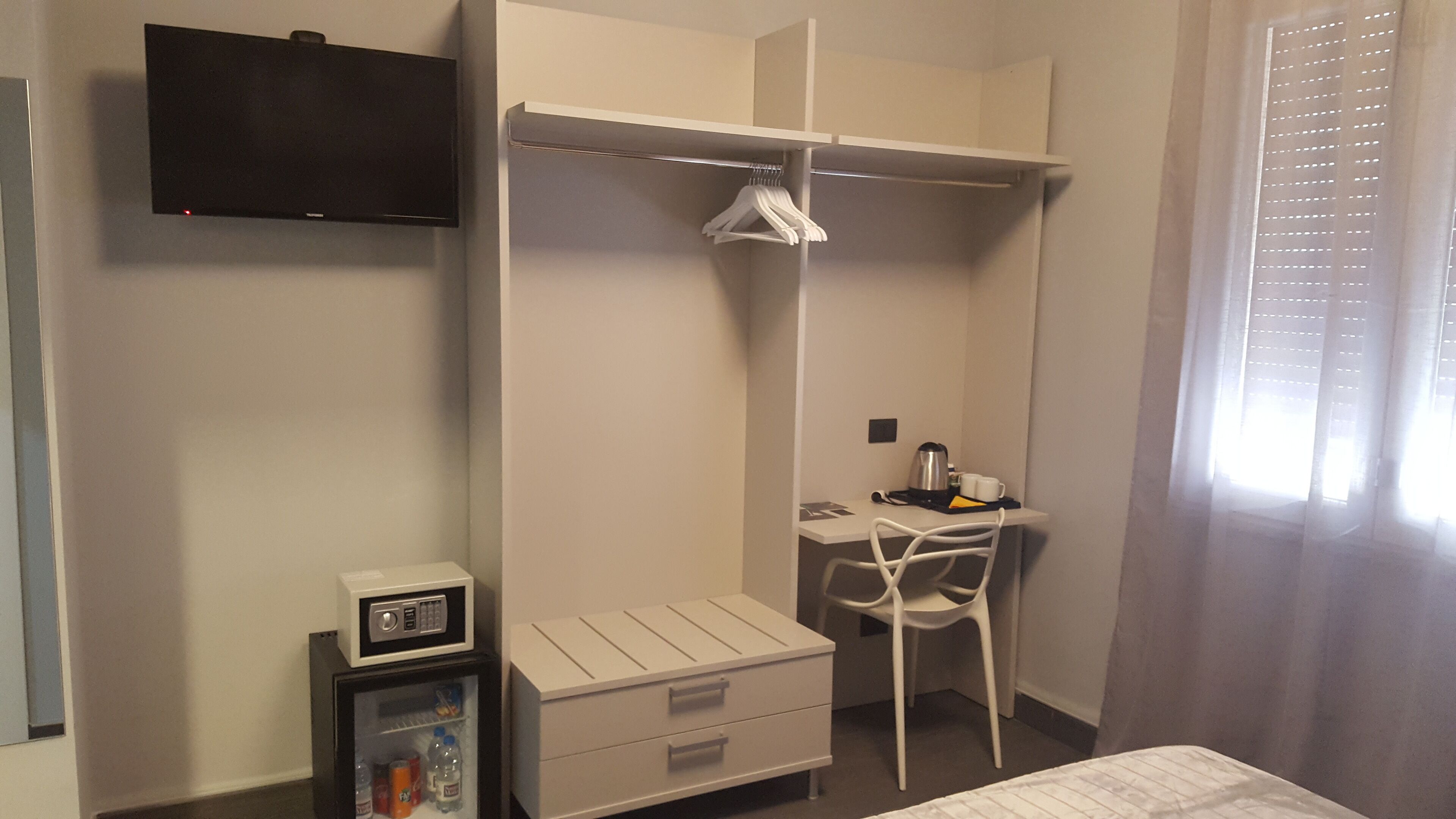 A bedroom with a bed, a desk with a chair, a wardrobe, a TV, and a mini-fridge.