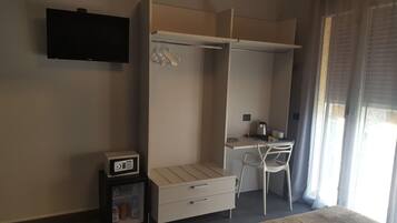 Habitación pequeña con cama, escritorio con silla, armario, televisor montado en la pared y refrigerador compacto.