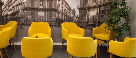 Une pièce décorée d’une fresque représentant des bâtiments historiques, avec des chaises jaunes et une plante en pot.