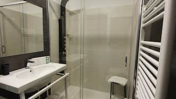 Un baño moderno con cabina de ducha de vidrio, un lavamanos blanco y un toallero empotrado.