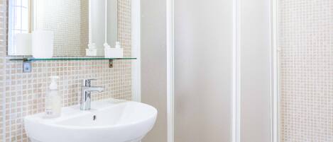 Un baño con un lavabo blanco, un estante de vidrio con artículos de aseo y una pared de azulejos.