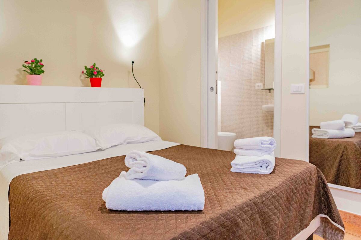 A hotel room with a brown bedspread, white pillows, and two potted plants on the headboard.