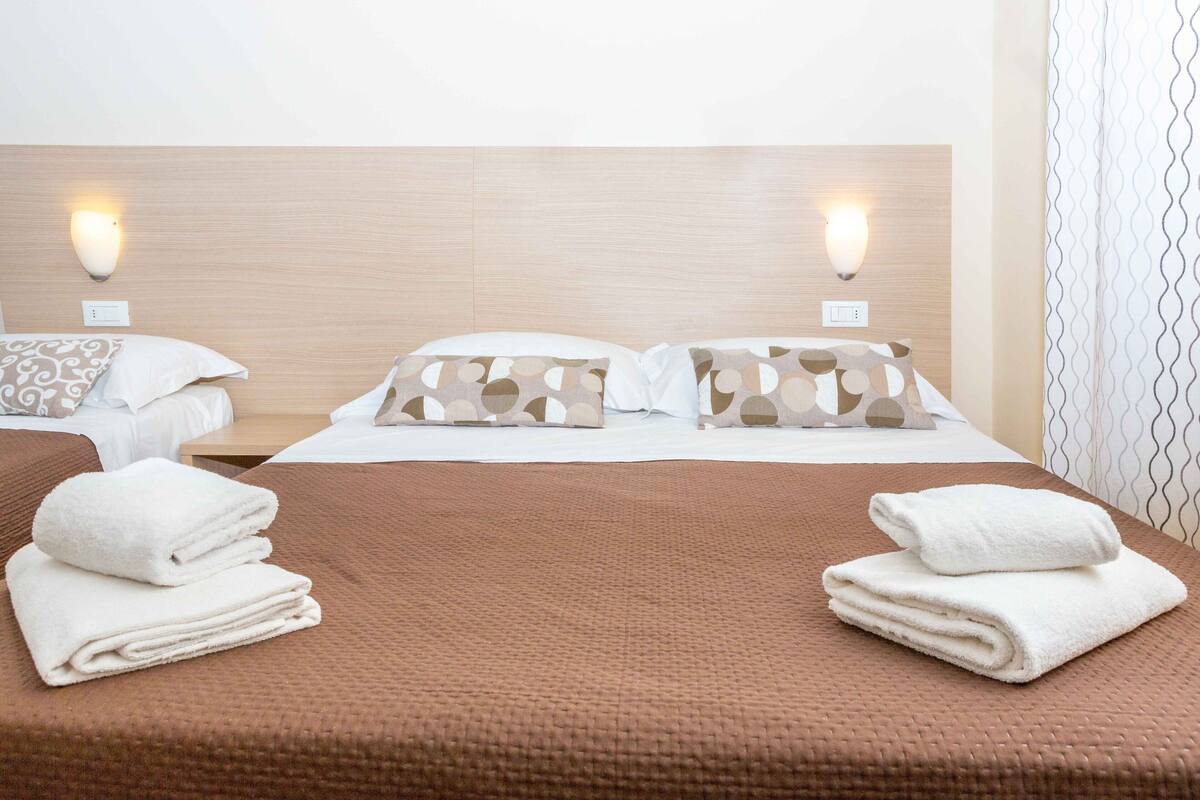 A hotel room with a brown bedspread, two pillows with a circular pattern, and two white towels on the bed.