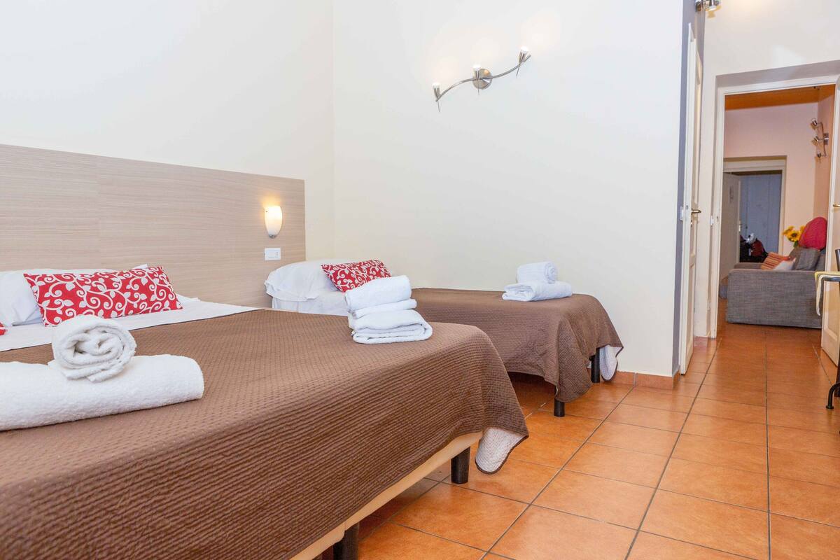A hotel room with two beds, each with a brown bedspread and a red and white patterned pillow. There are towels neatly folded on each bed.