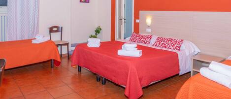 A hotel room with two beds, each with an orange bedspread and white pillows, a chair, a small table, and a wall-mounted light.