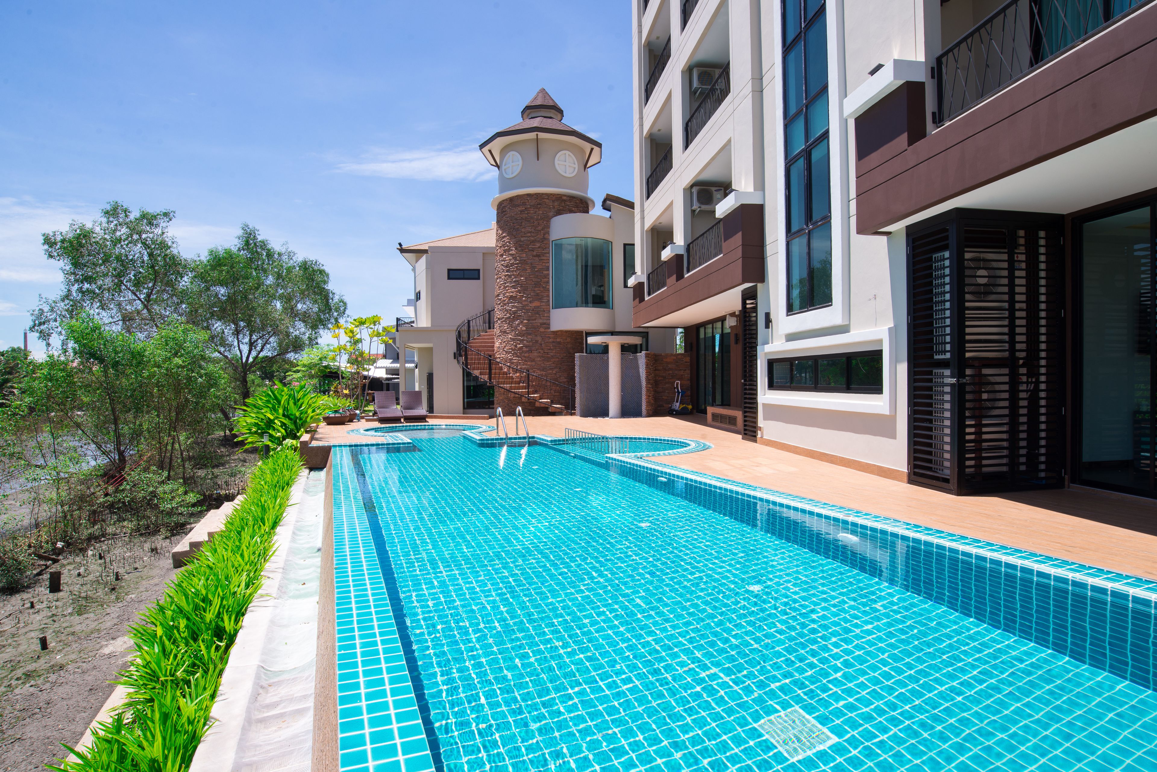 Un hotel moderno con piscina, una estructura similar a una torre y una zona ajardinada con árboles.