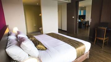 Une chambre d’hôtel moderne avec un grand lit, une lampe de chevet et une vue sur la cuisine et l’espace repas, grâce à une porte ouverte.