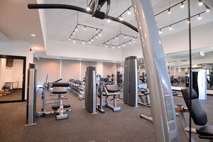 Un gimnasio con diversas máquinas de ejercicio, espejos e iluminación colgante en el techo.