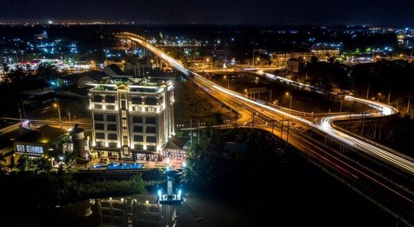A multi-level hotel with a prominent building, a parking area, and a road with light trails indicating traffic. - Coco View Hotel (Samut Songkhram)