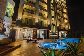 A modern hotel with a swimming pool, multiple balconies, and a well-lit exterior.