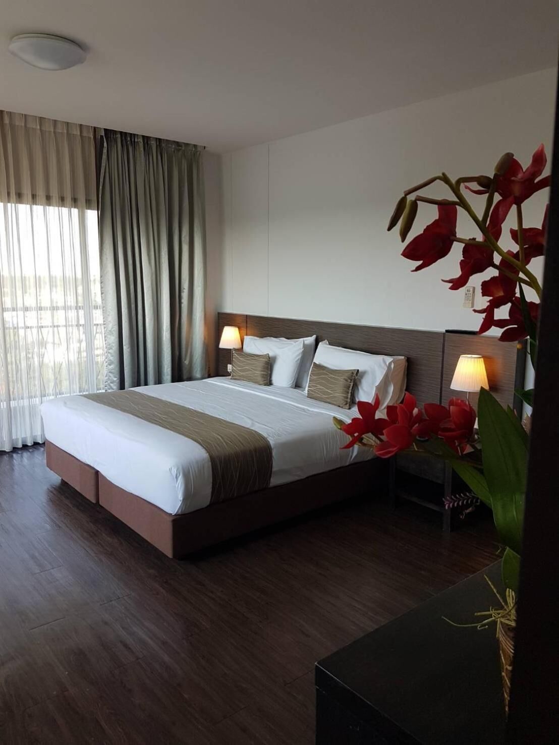 A hotel room with a large bed, two bedside tables with lamps, a wooden headboard, and a large window with curtains.