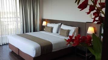 A hotel room with a large bed, two bedside tables with lamps, a wooden headboard, and a large window with curtains.
