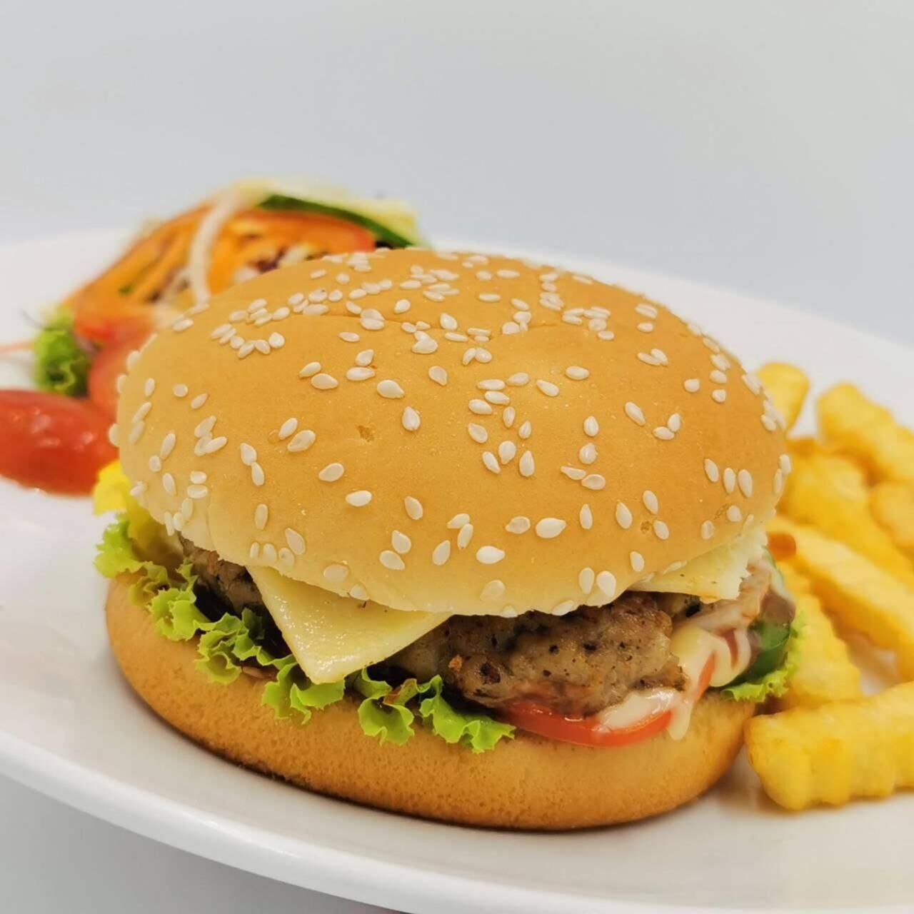 A hamburger with lettuce, cheese, and a sesame seed bun, accompanied by French fries and a side salad.