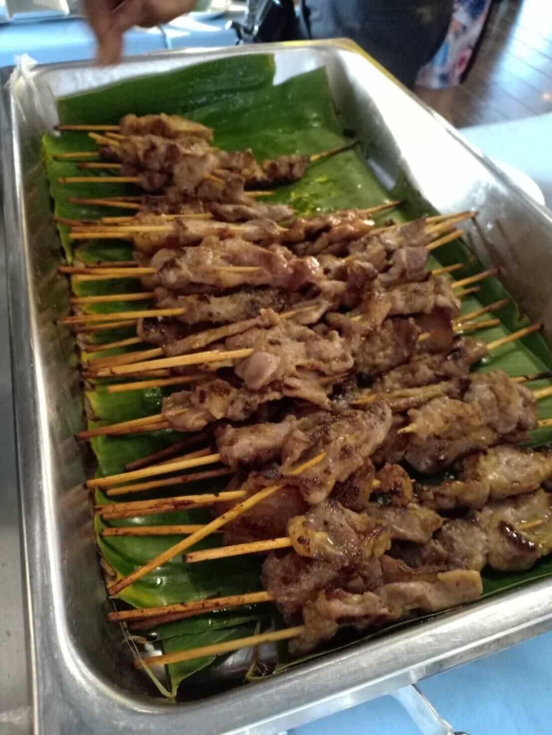 A tray of skewered meat on a metal surface with a green leaf underneath.