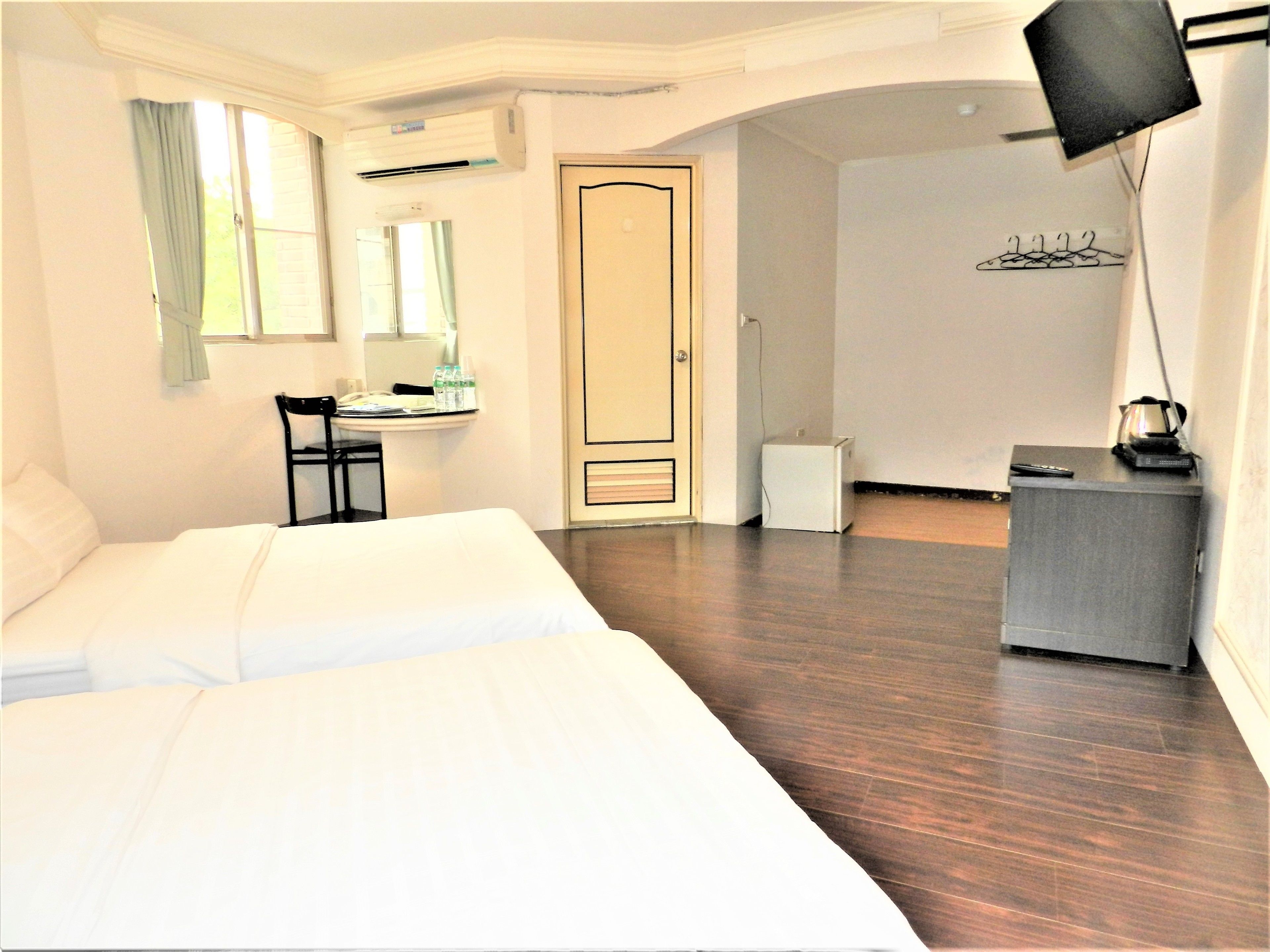 Habitación de hotel con cama, escritorio, silla, aire acondicionado, puerta y una pequeña kitchenette.
