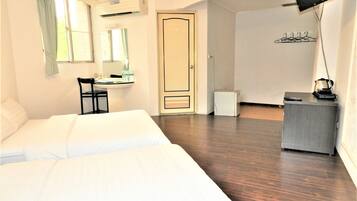 Habitación de hotel con cama, escritorio, silla, aire acondicionado, puerta y una pequeña kitchenette.