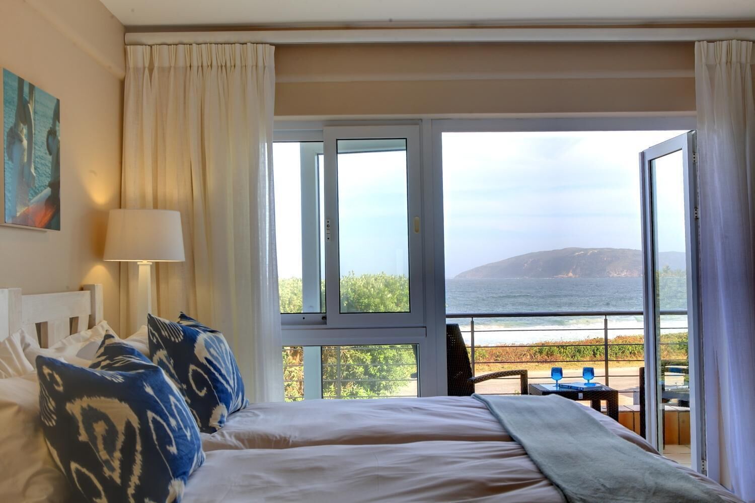 Quarto de hotel com uma cama, uma luminária e vista para o oceano.