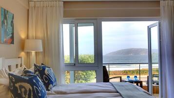 Quarto de hotel com uma cama, uma luminária e vista para o oceano.