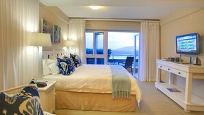 A hotel room with a bed, a desk, a chair, a TV, and a view of the outdoors. - Periwinkle Guest Lodge (Plettenberg Bay)