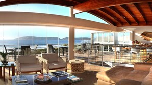 A spacious living area with a view of the sea, featuring a wooden ceiling, large windows, and modern furniture. - Periwinkle Guest Lodge (Plettenberg Bay)