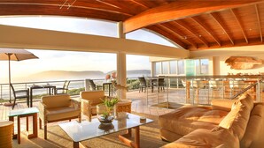 A spacious outdoor seating area with a view of the ocean, furnished with sofas, chairs, and a table. - Periwinkle Guest Lodge (Plettenberg Bay)
