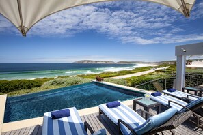 A poolside area with lounge chairs and a view of the ocean. - Periwinkle Guest Lodge (Plettenberg Bay)