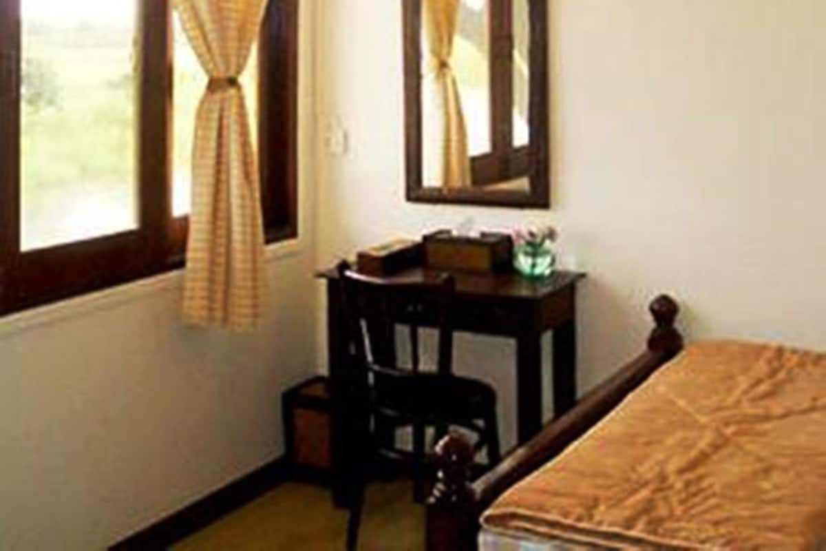 A bedroom with a bed, a desk, a chair, a ceiling fan, and a window with curtains.