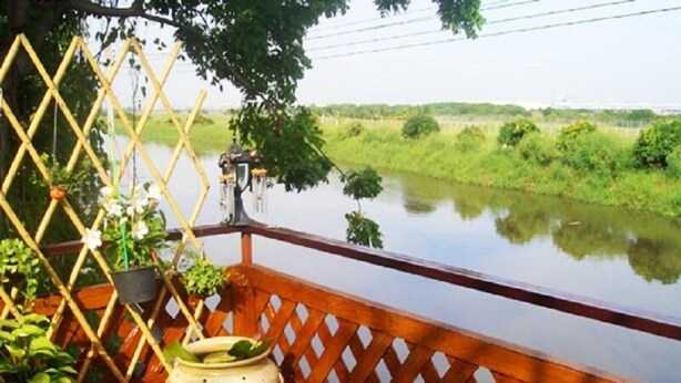A wooden balcony with a lattice railing overlooking a calm river, surrounded by greenery. - YHA Bangkok Airport - Hostel (Bang Phli)