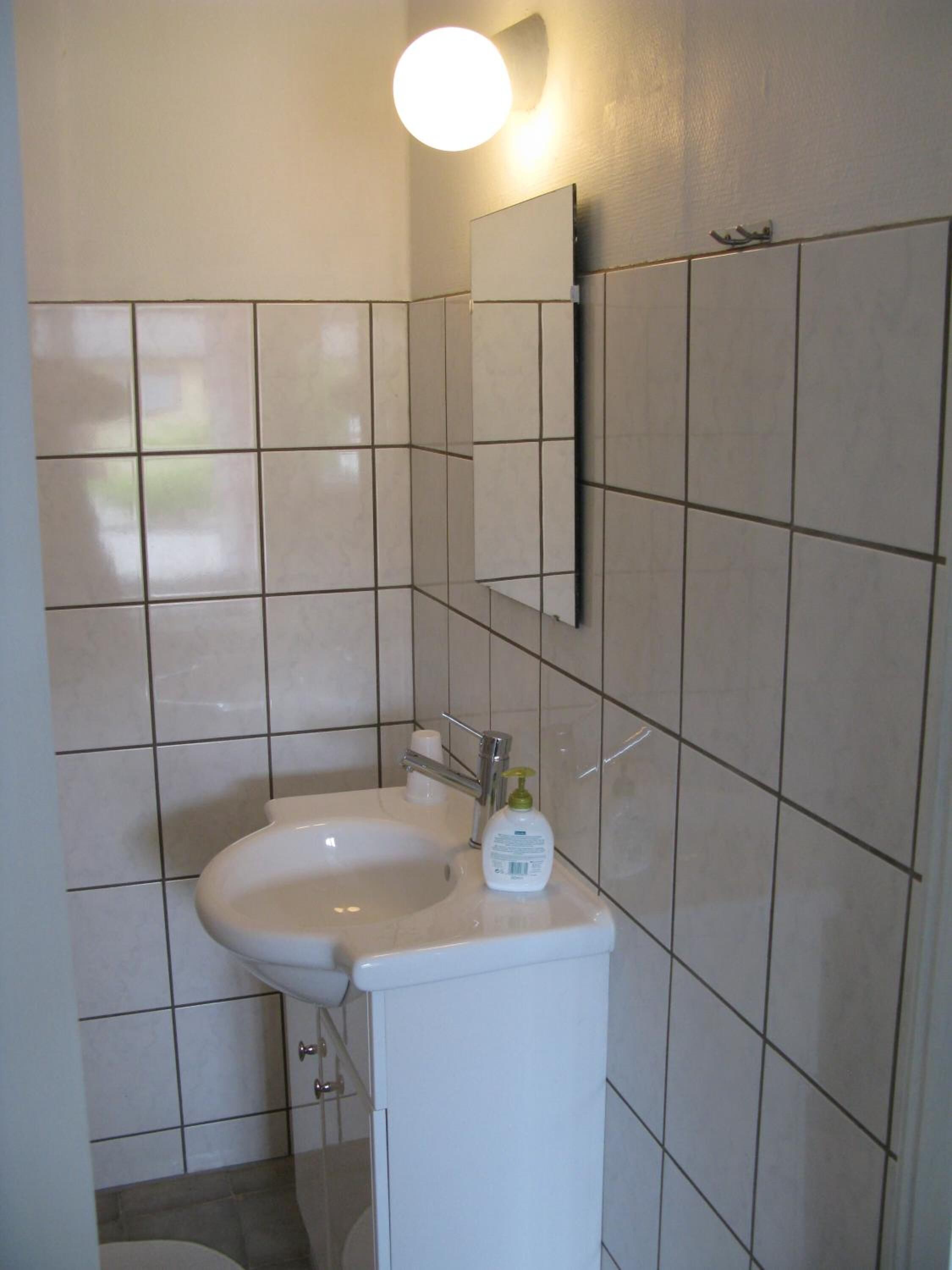 Un baño con un lavabo blanco, un espejo y una lámpara en la pared.