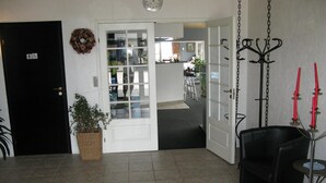 A room with a black door, a white door leading to a kitchen, a black chair, a small round table, and a hanging light fixture. - Motel Europa (Svenstrup)