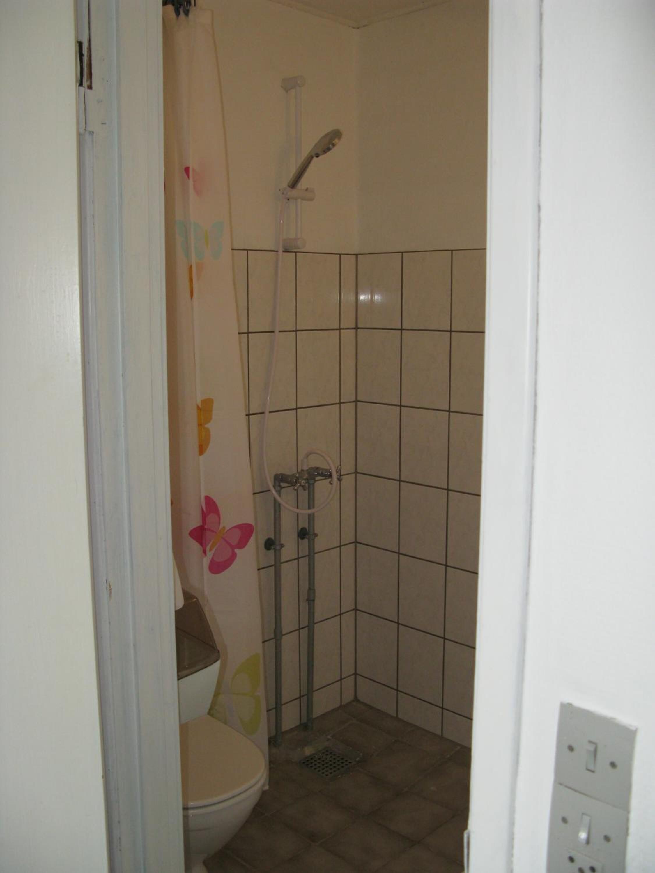 A small, tiled bathroom with a toilet, a shower, and a wall with a floral design.
