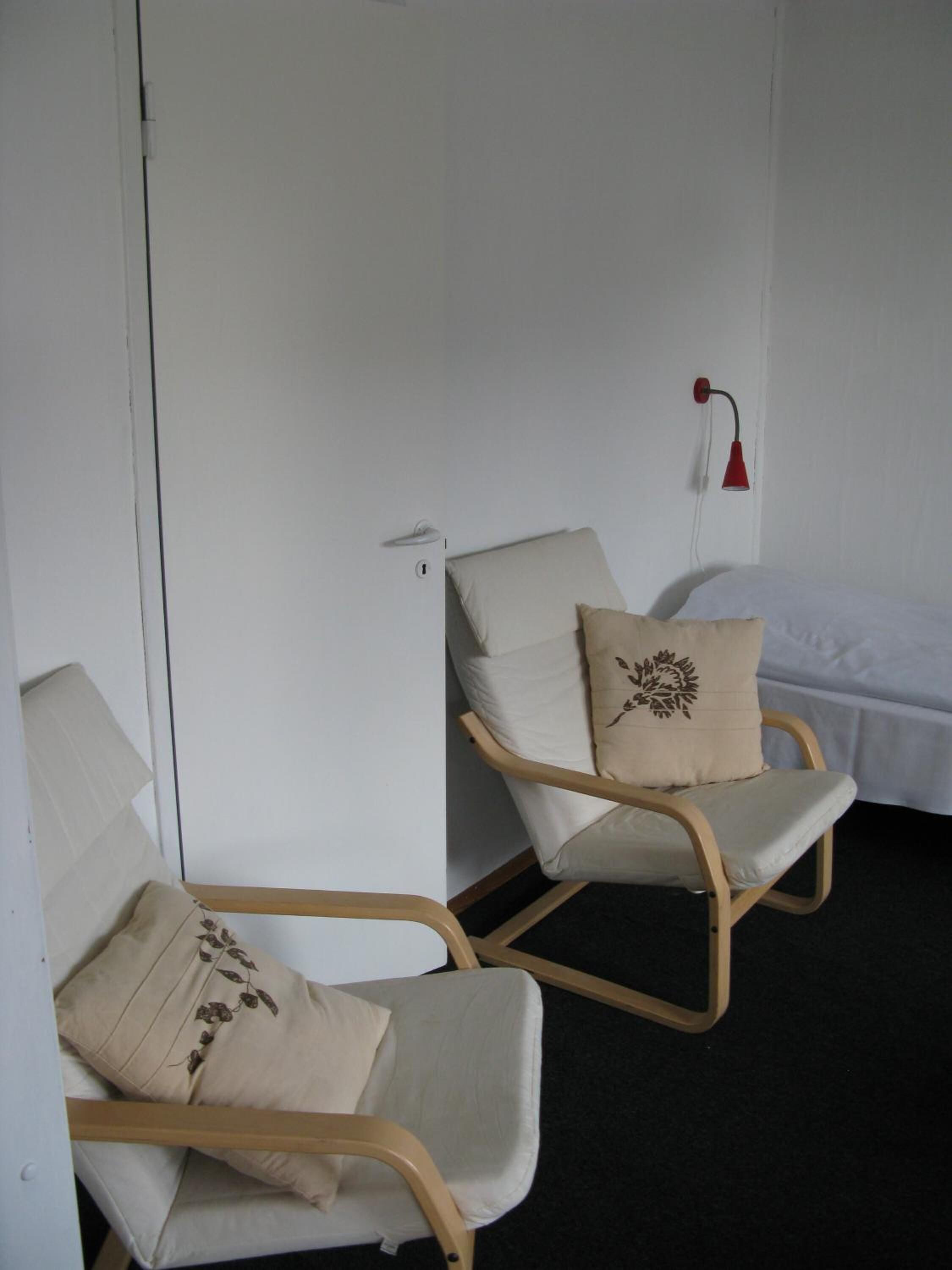 Una habitación con dos mecedoras, una cama y una lámpara de pared roja.