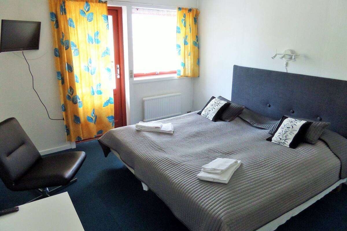 A hotel room with a bed, a chair, a TV, and a window with curtains.