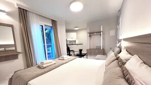 A hotel room with a large bed, a desk, a chair, a wardrobe, and a view of the outdoors. - Sea Breeze (Chania)