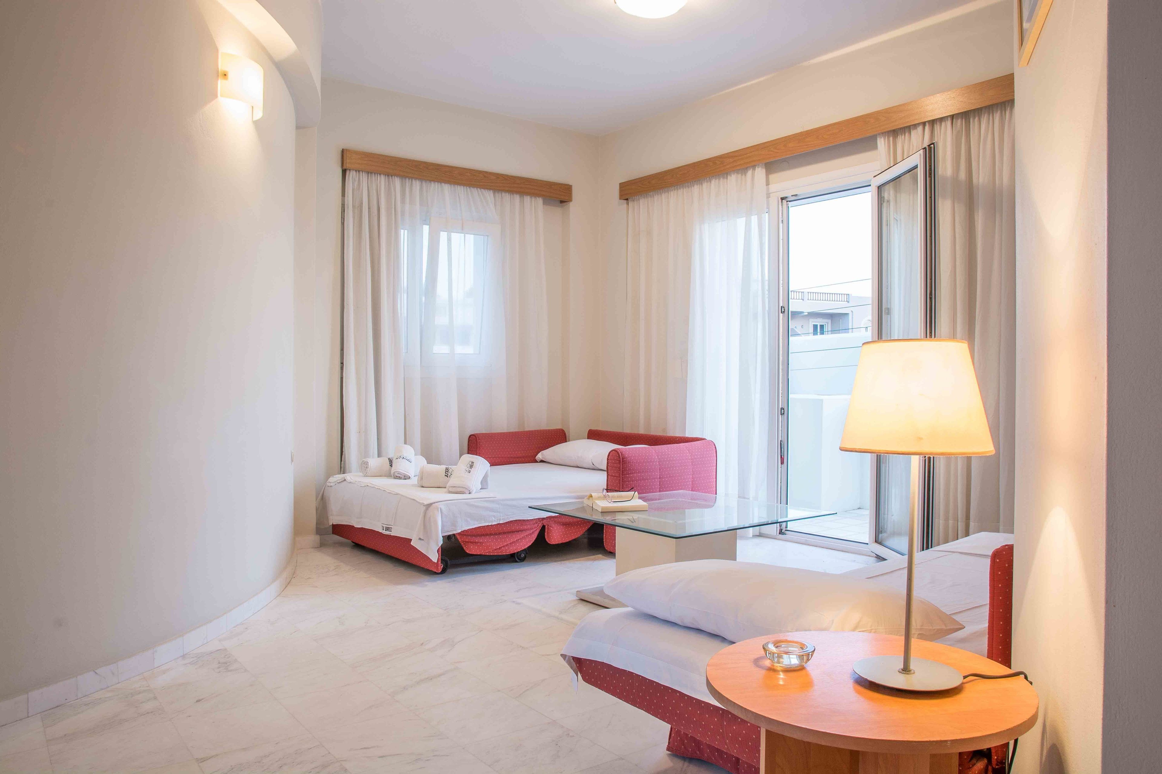 A hotel room with a bed, a sofa, a table with a lamp, and a window with curtains.