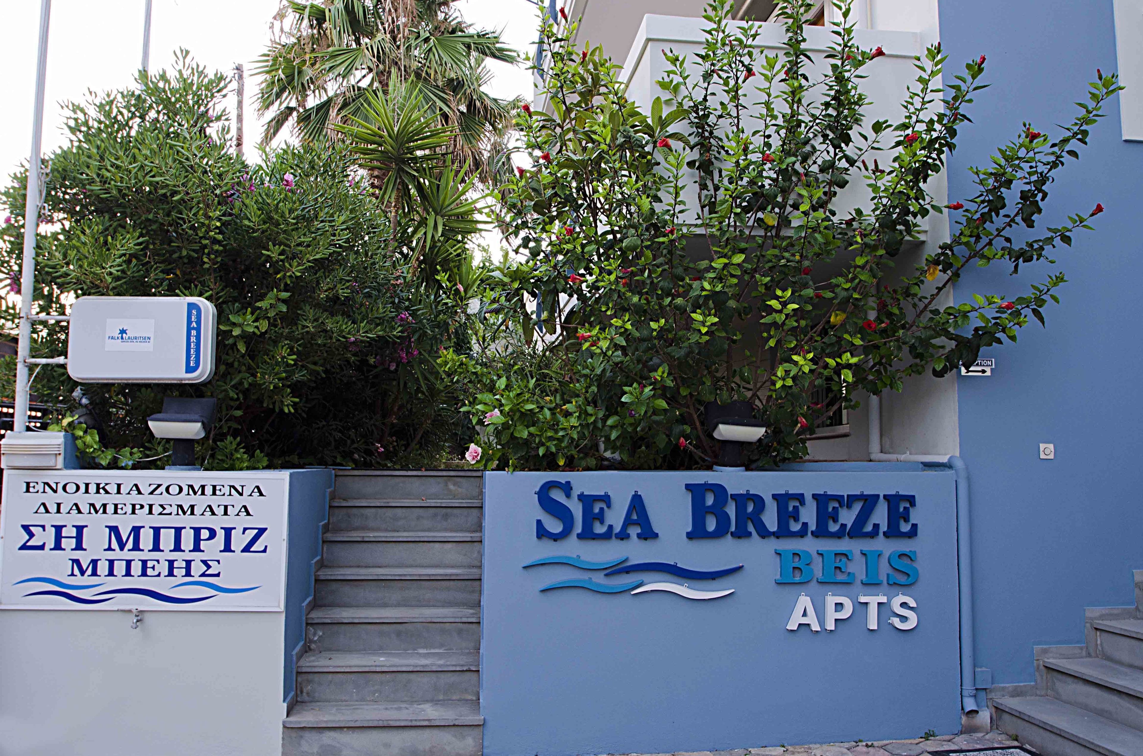 Un immeuble avec une enseigne indiquant « Sea Breeze Apts » et une autre enseigne avec du texte en grec.