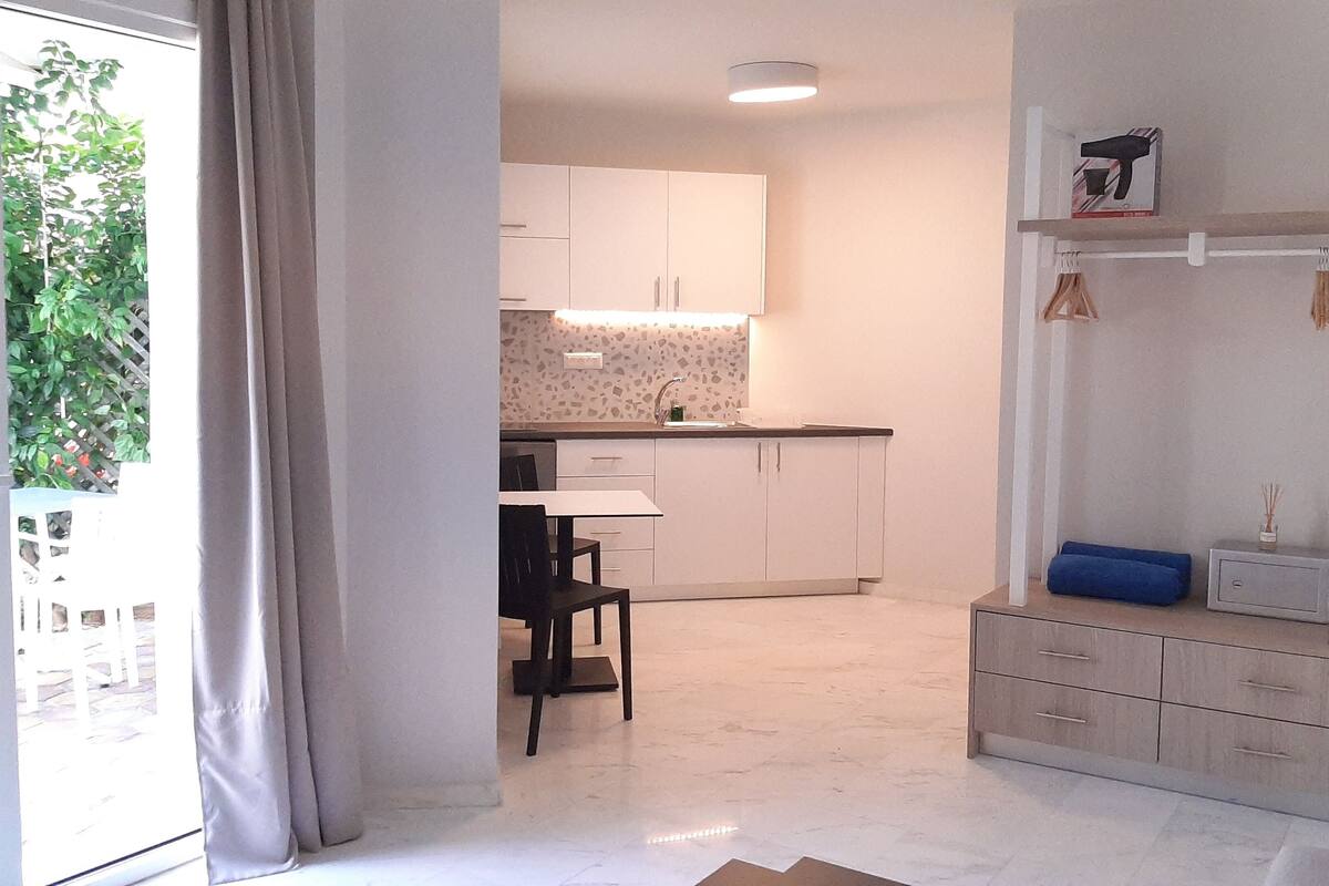 A modern kitchen with white cabinets, a dining area with a table and chairs, and a built-in wardrobe with drawers.