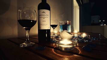A bottle of Merlot wine, two wine glasses, a candle, and a small bowl on a wooden table.