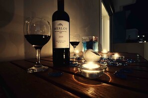Une bouteille de vin rouge Merlot, deux verres à vin, une bougie et un petit bol sur une table en bois.