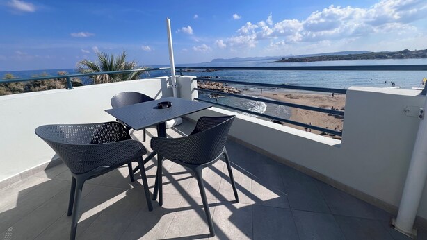 A terrace with a table and chairs overlooking a beach. - Sea Breeze (Chania)
