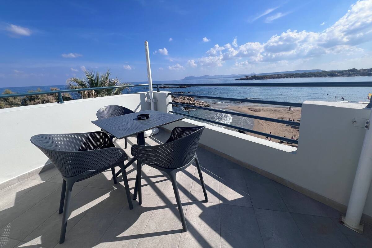 A terrace with a table and chairs overlooking a beach.