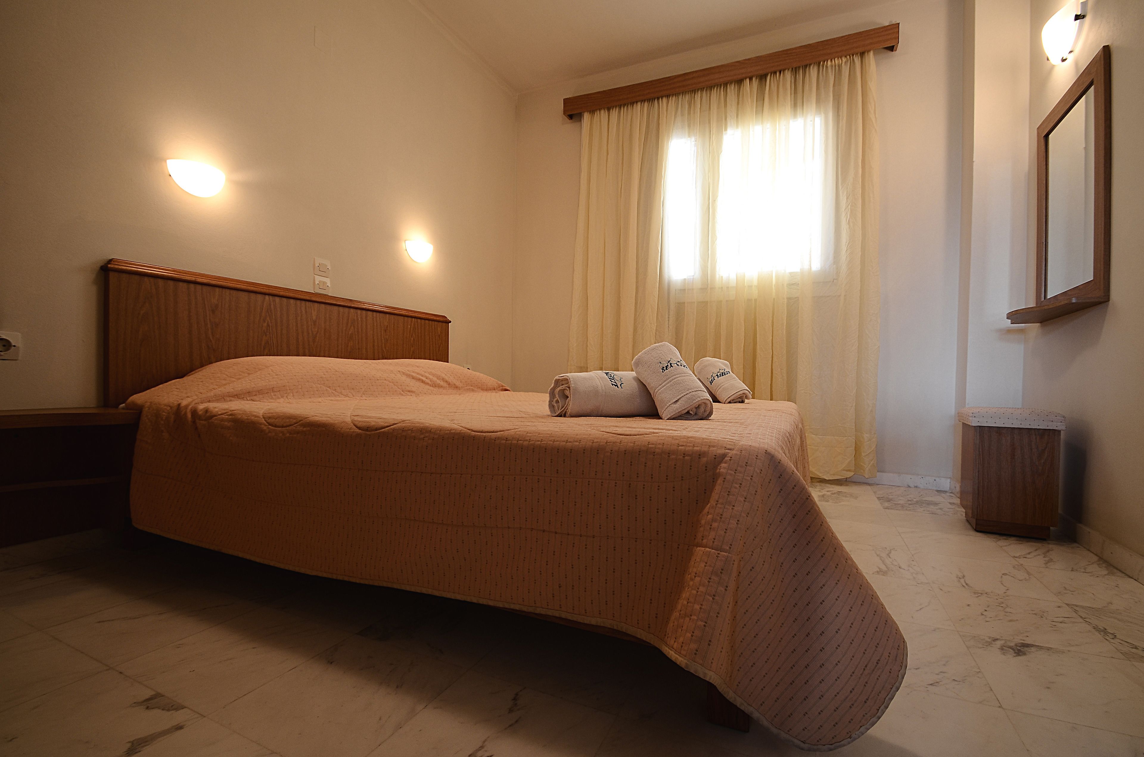 A neatly made bed with a headboard, a bedside table, and a window with curtains.