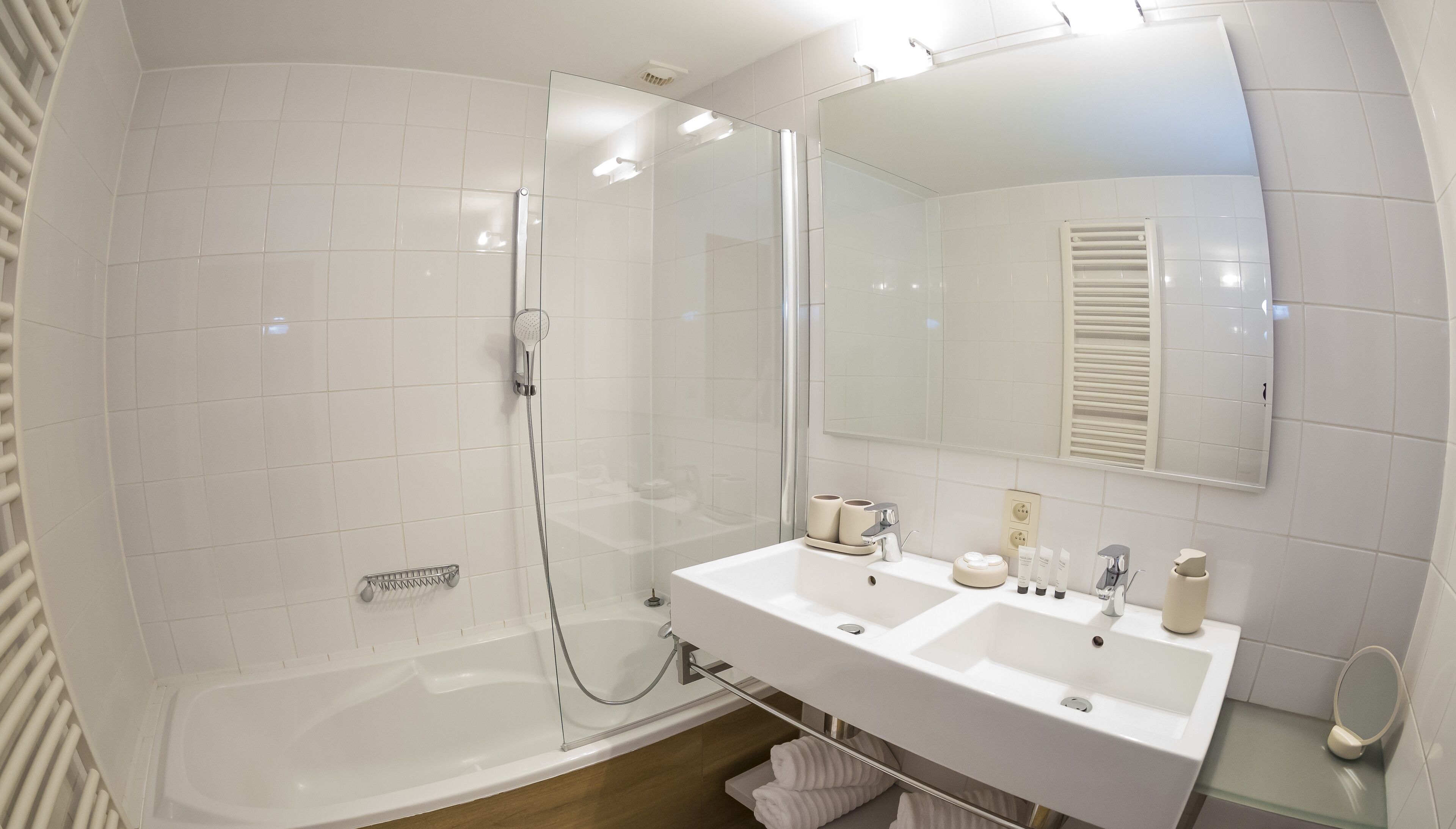Un baño moderno con ducha de vidrio, lavamanos blanco doble y un espejo grande.